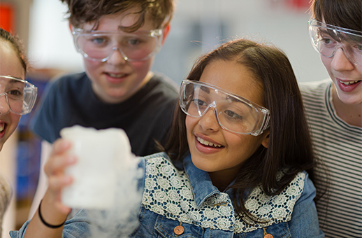 Middle school students wearing protective goggles while observing a smoking beaker