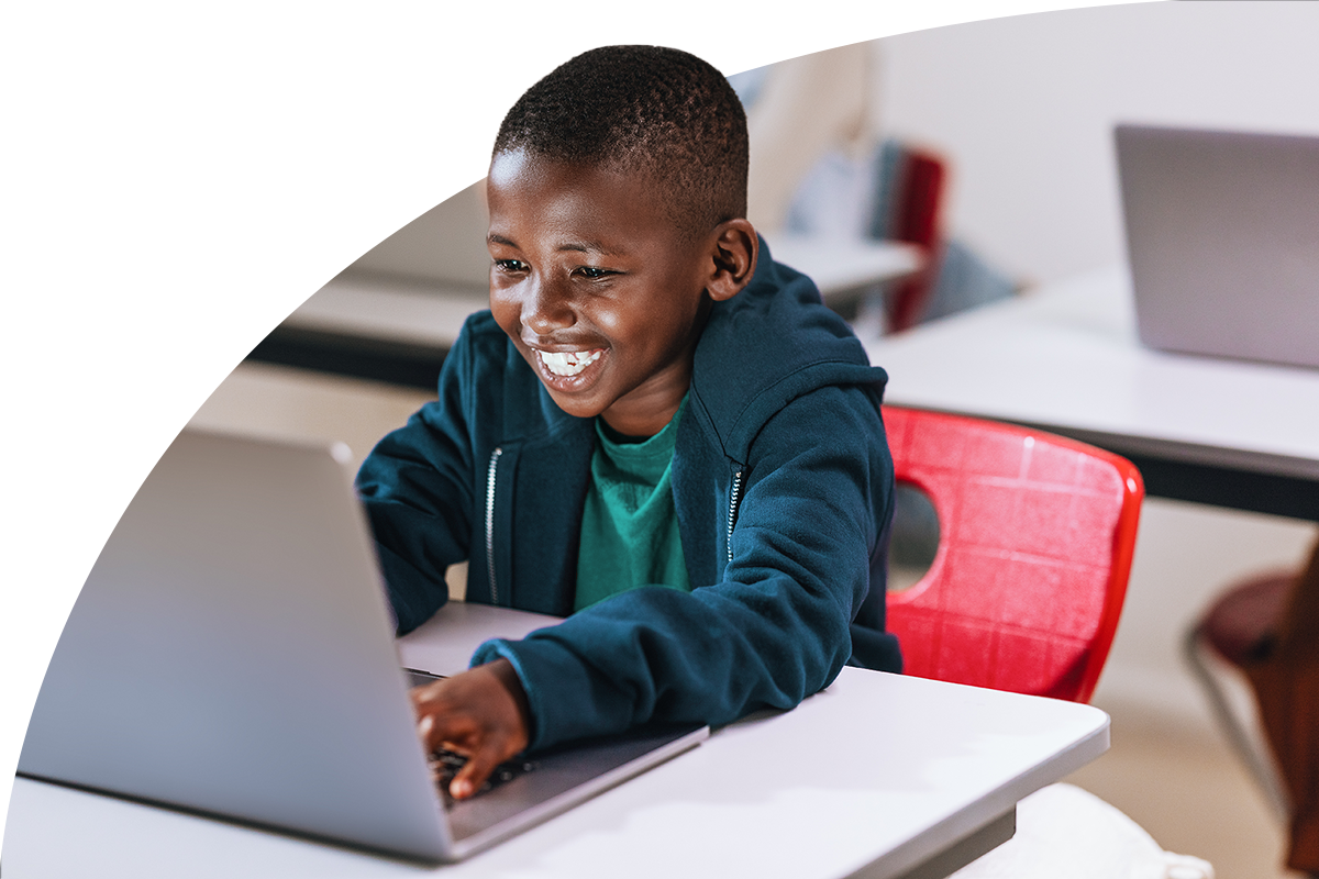 Young student smiling and typing on laptop while sitting at classroom desk
